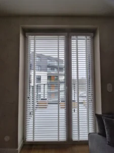 Białe żaluzje zamontowane na podwójnym oknie balkonowym, zapewniające prywatność w nowoczesnym apartamencie. Realizacja w Poznaniu.